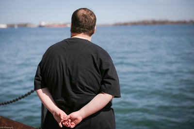 Man living with obesity holds his hands behind his back while looking at a body of water.