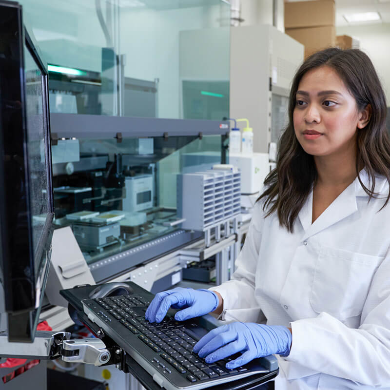 A female researcher typing on a computer in a lab.